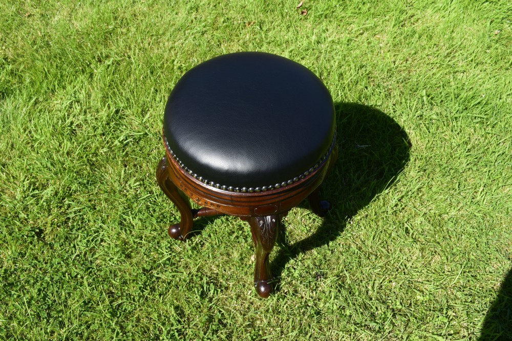 A Victorian walnut piano stool with a circular black leather upholstered swivel seat resting on four carved cabriole legs. View II
