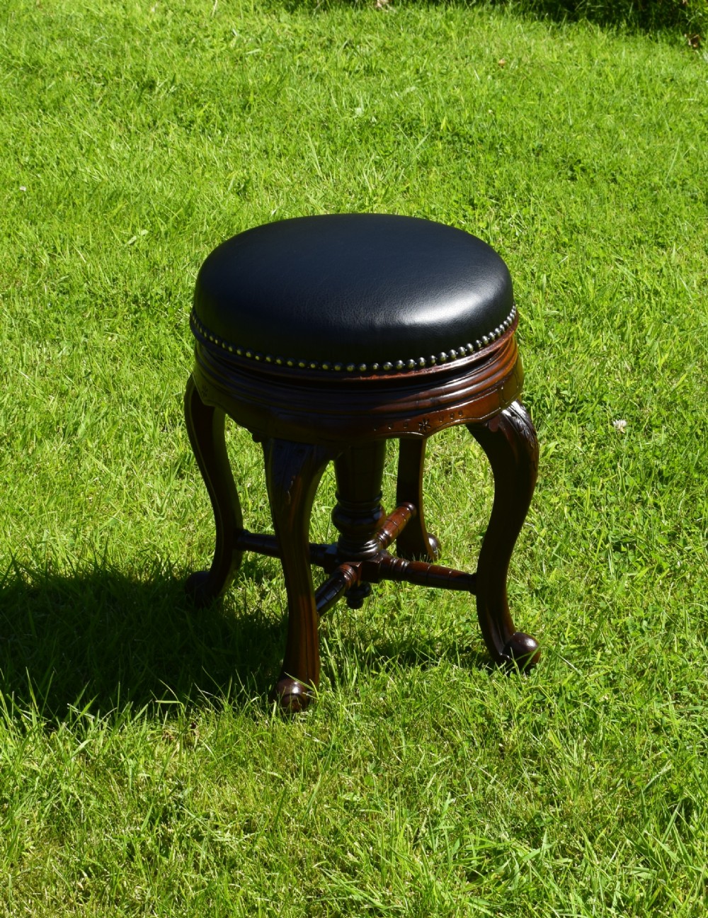 A Victorian walnut piano stool with a circular black leather upholstered swivel seat resting on four carved cabriole legs. View III
