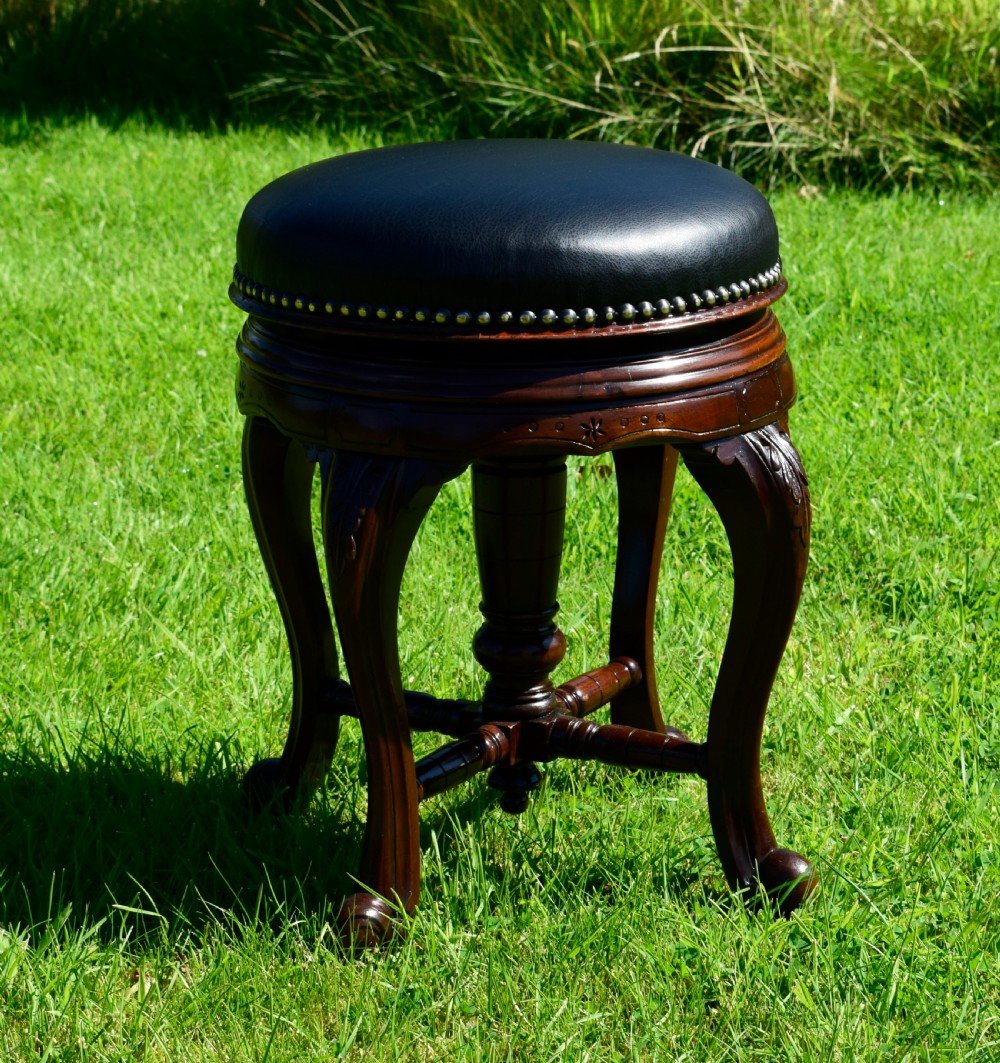 A Victorian walnut piano stool with a circular black leather upholstered swivel seat resting on four carved cabriole legs. View V