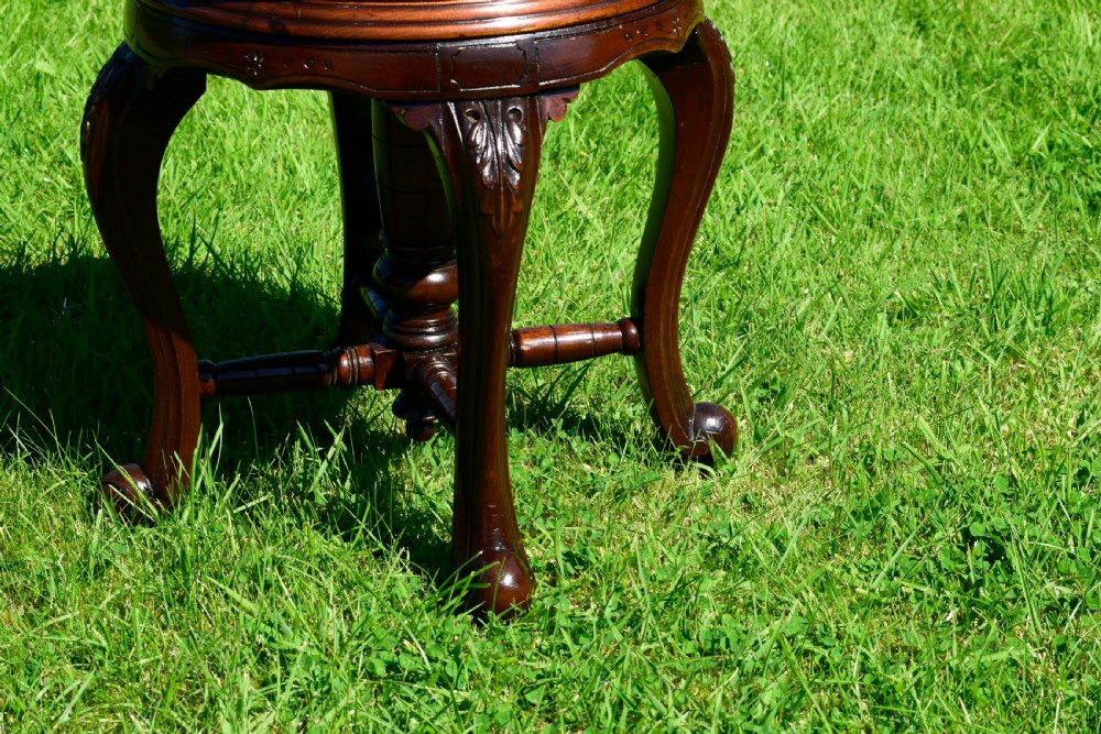 A Victorian walnut piano stool with a circular black leather upholstered swivel seat resting on four carved cabriole legs. View VI