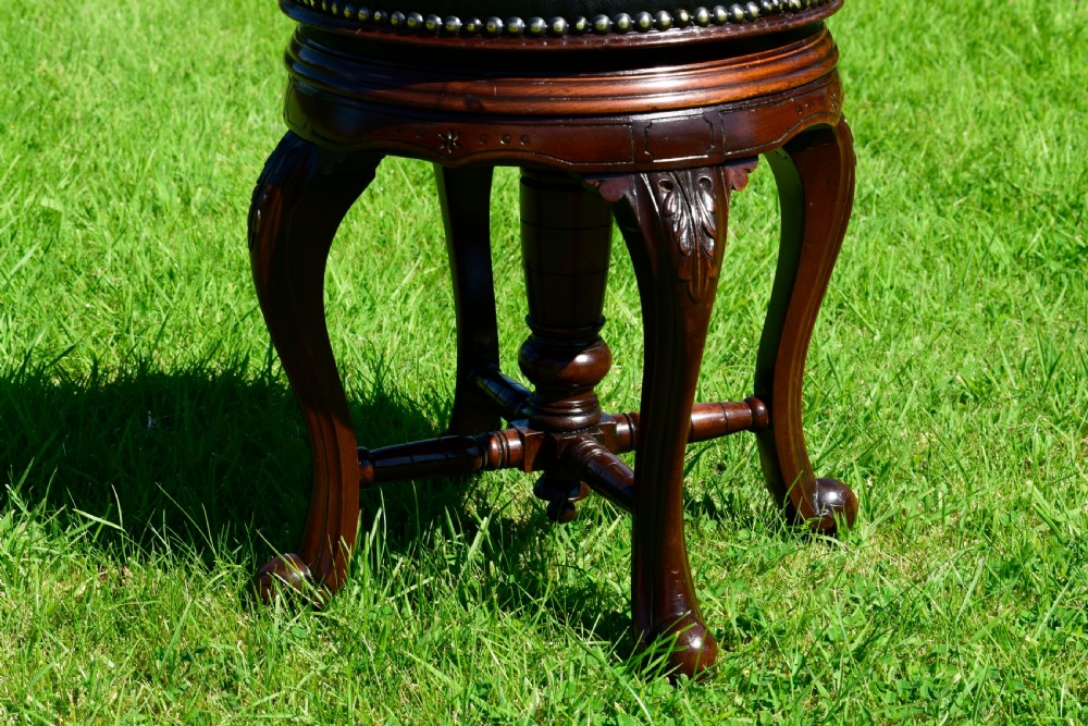 A Victorian walnut piano stool with a circular black leather upholstered swivel seat resting on four carved cabriole legs. View VII