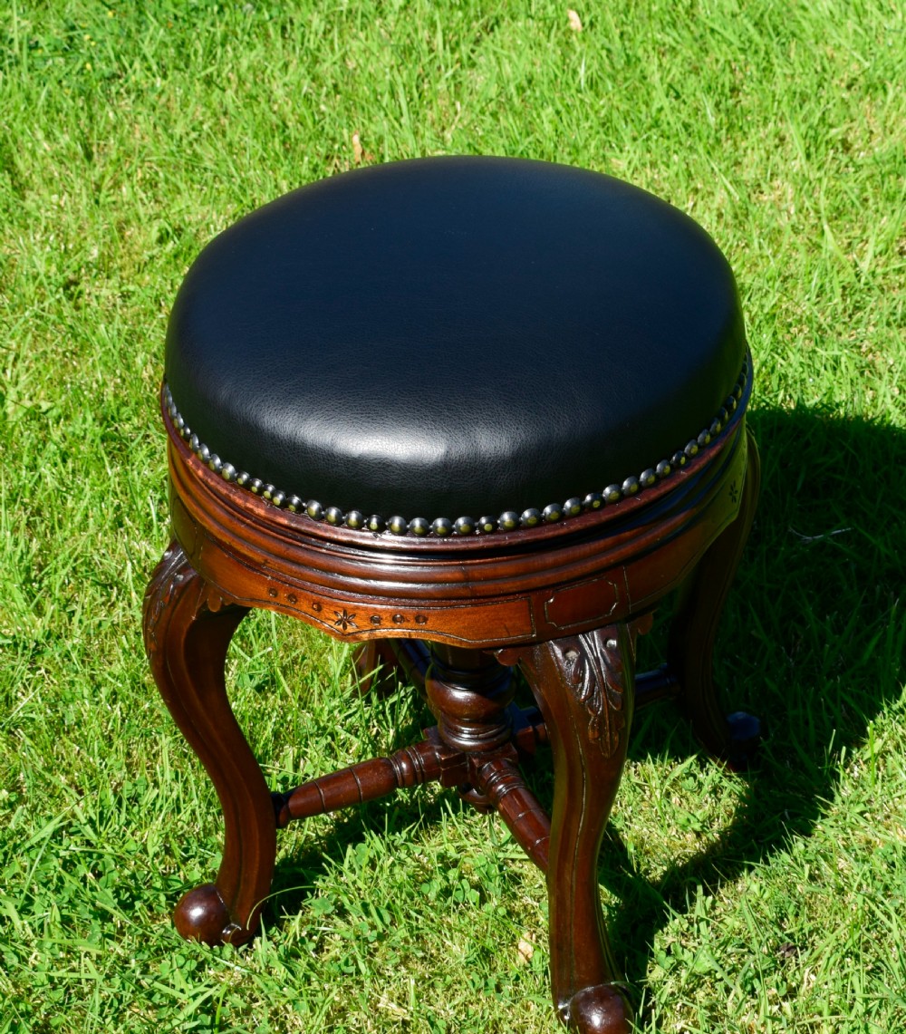 A Victorian walnut piano stool with a circular black leather upholstered swivel seat resting on four carved cabriole legs. View VIII