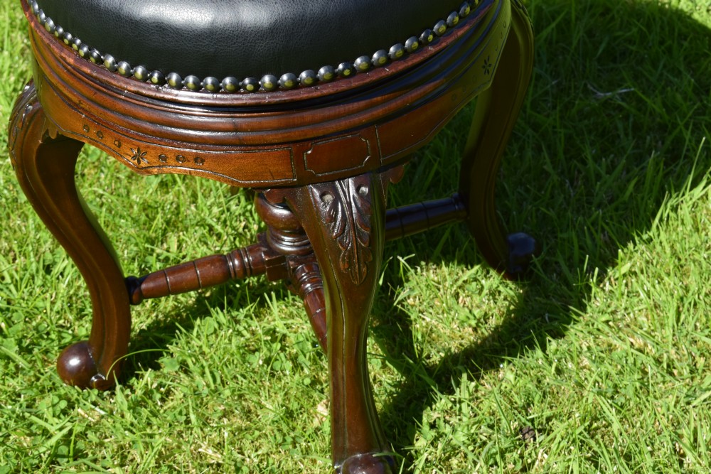 A Victorian walnut piano stool with a circular black leather upholstered swivel seat resting on four carved cabriole legs. View IX