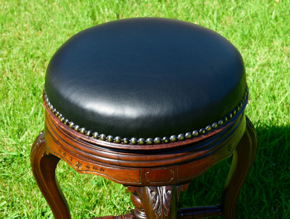 A Victorian walnut piano stool with a circular black leather upholstered swivel seat resting on four carved cabriole legs. View X