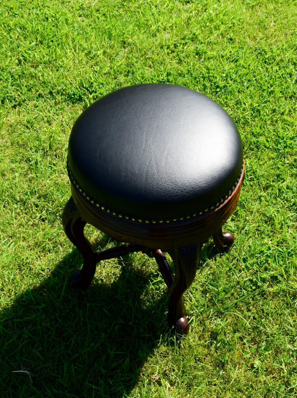 A Victorian walnut piano stool with a circular black leather upholstered swivel seat resting on four carved cabriole legs. View XI