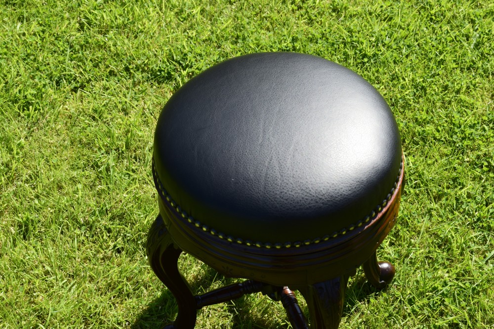 A Victorian walnut piano stool with a circular black leather upholstered swivel seat resting on four carved cabriole legs. View XII