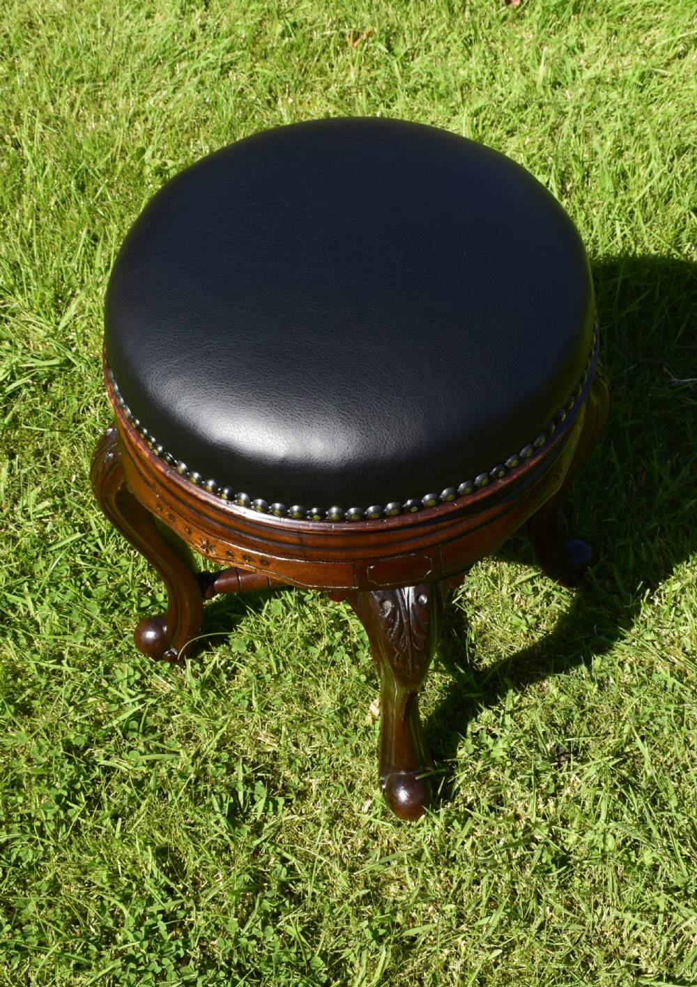 A Victorian walnut piano stool with a circular black leather upholstered swivel seat resting on four carved cabriole legs. View XIII