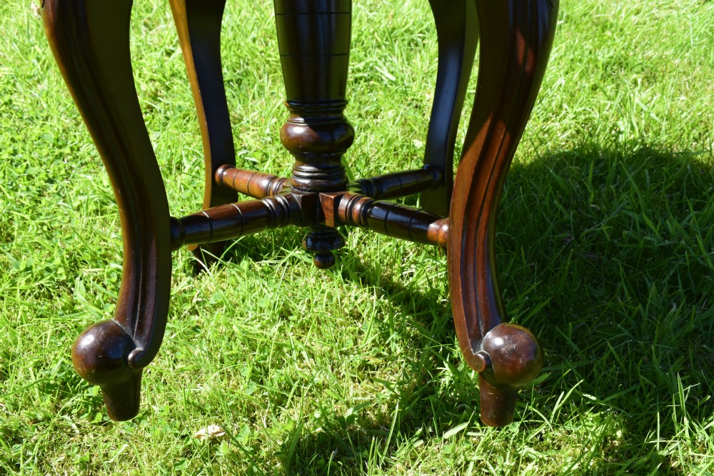 A Victorian walnut piano stool with a circular black leather upholstered swivel seat resting on four carved cabriole legs. View XV