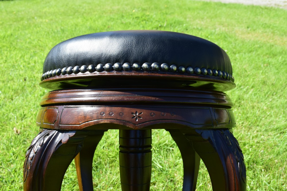 A Victorian walnut piano stool with a circular black leather upholstered swivel seat resting on four carved cabriole legs. View XVI