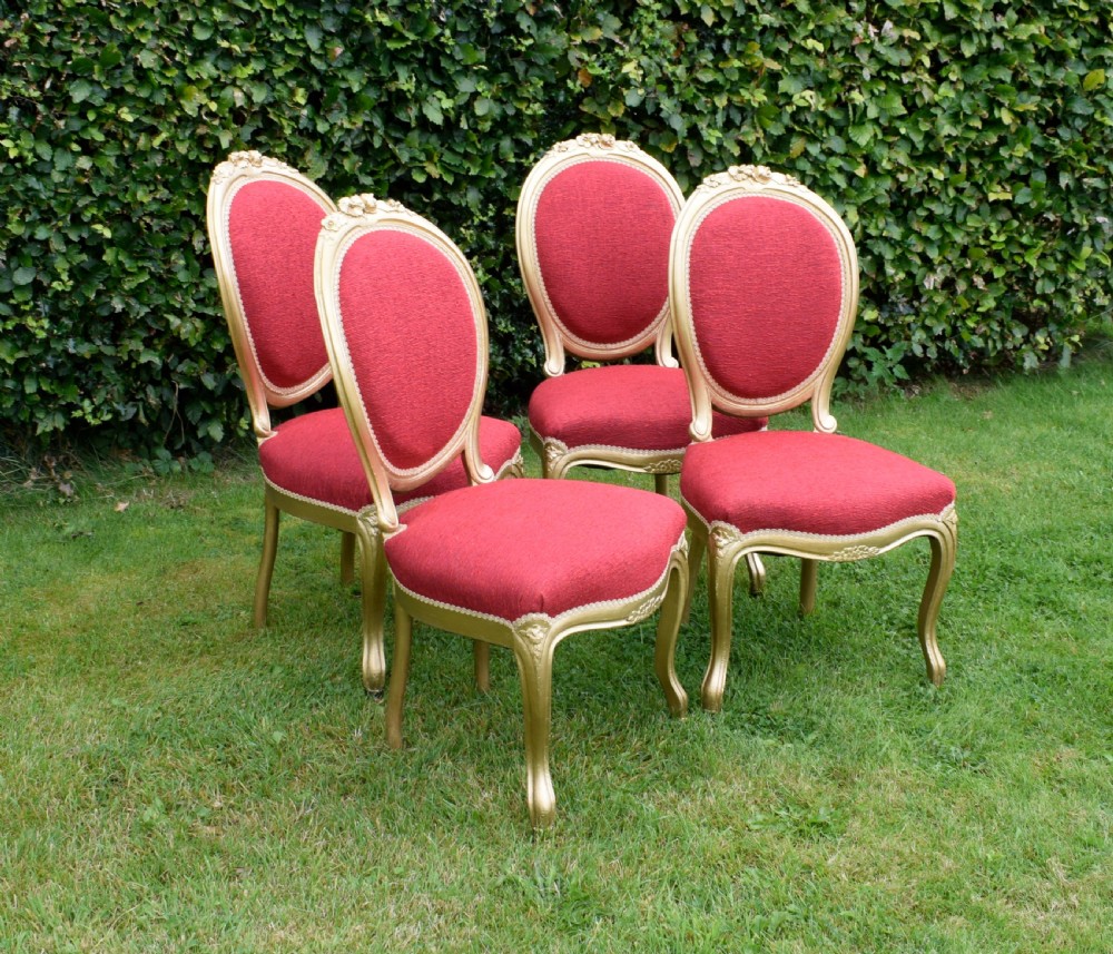A set of four French-style dining chairs featuring gold-painted frames with carved oval backs and red woven fabric upholstery.