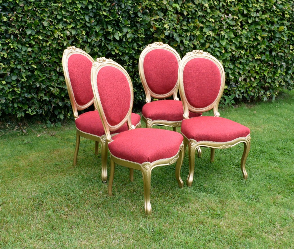 A set of four French-style dining chairs featuring gold-painted frames with carved oval backs and red woven fabric upholstery. View III