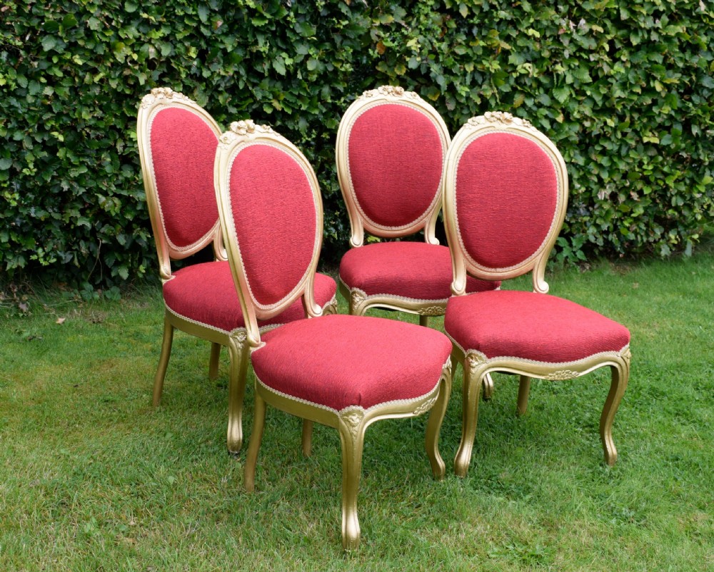 A set of four French-style dining chairs featuring gold-painted frames with carved oval backs and red woven fabric upholstery. View IV