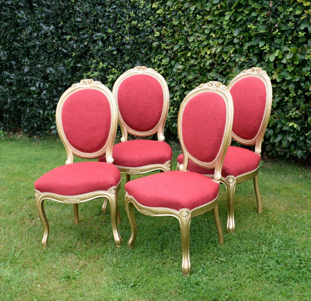 A set of four French-style dining chairs featuring gold-painted frames with carved oval backs and red woven fabric upholstery. View V