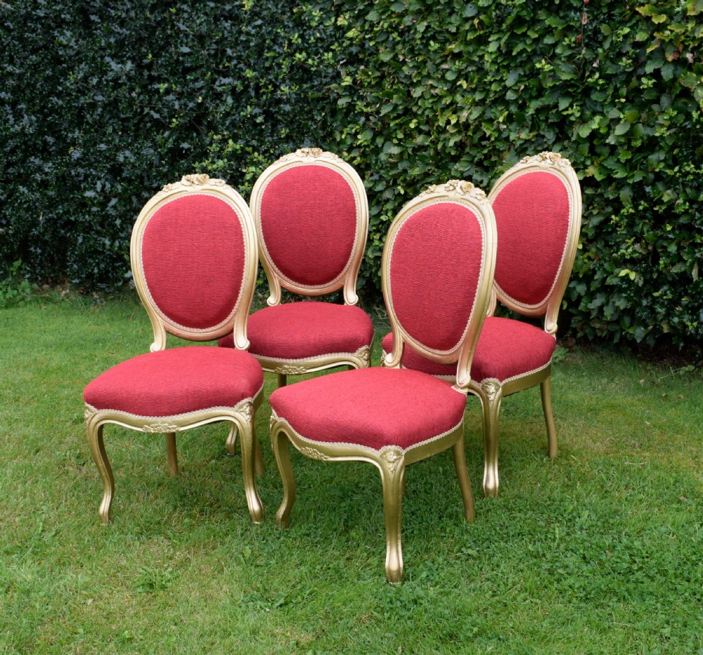 A set of four French-style dining chairs featuring gold-painted frames with carved oval backs and red woven fabric upholstery. View VI