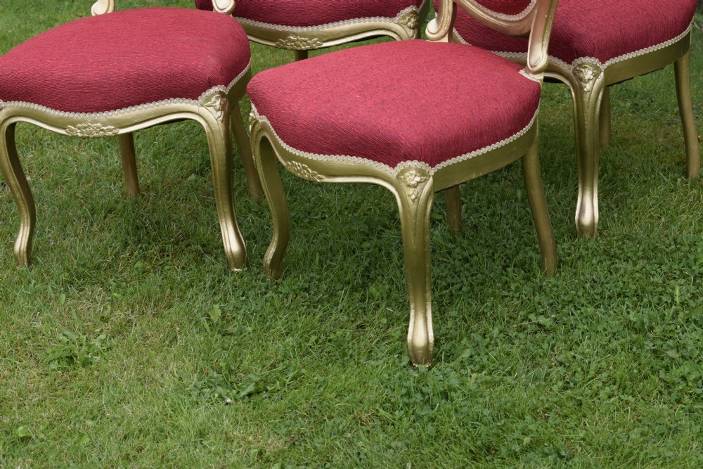 A set of four French-style dining chairs featuring gold-painted frames with carved oval backs and red woven fabric upholstery. View VII