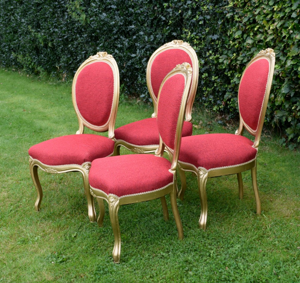 A set of four French-style dining chairs featuring gold-painted frames with carved oval backs and red woven fabric upholstery. View IX