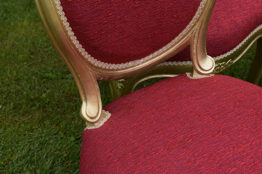 A set of four French-style dining chairs featuring gold-painted frames with carved oval backs and red woven fabric upholstery. View XI