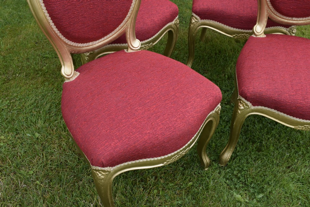 A set of four French-style dining chairs featuring gold-painted frames with carved oval backs and red woven fabric upholstery. View XII