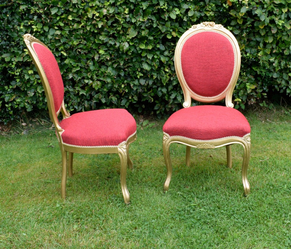 A set of four French-style dining chairs featuring gold-painted frames with carved oval backs and red woven fabric upholstery. View XV
