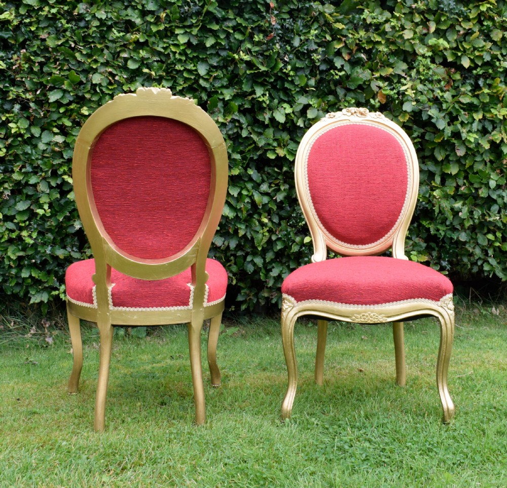 A set of four French-style dining chairs featuring gold-painted frames with carved oval backs and red woven fabric upholstery. View XVI