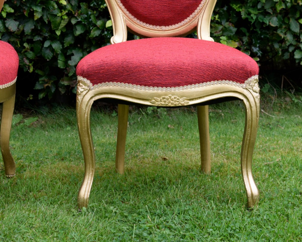 A set of four French-style dining chairs featuring gold-painted frames with carved oval backs and red woven fabric upholstery. View XVII