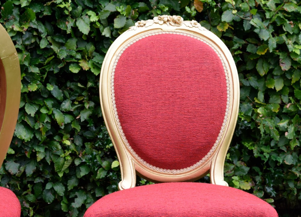 A set of four French-style dining chairs featuring gold-painted frames with carved oval backs and red woven fabric upholstery. View XVIII