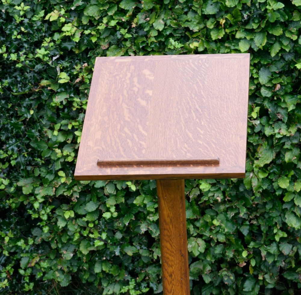 An early 20th-century solid oak floor-standing lectern featuring an angled book rest above a central column supported by a stepped cruciform base. View X