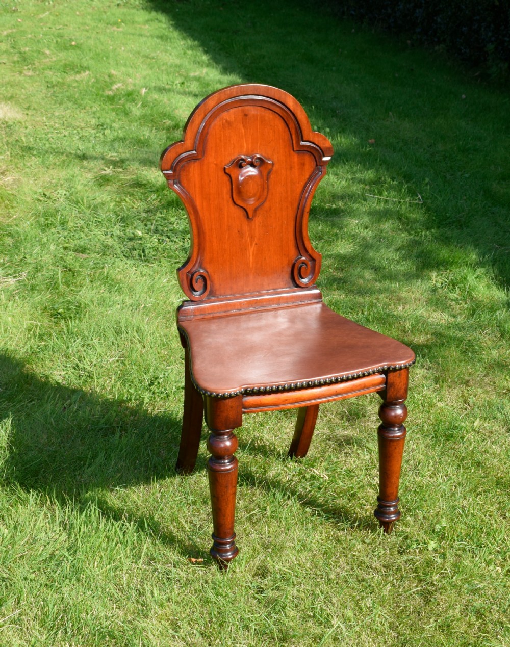 A Victorian mahogany hall chair with a carved shield-shaped backrest, stud-trimmed dark seat, turned front legs, and splayed rear legs. View II