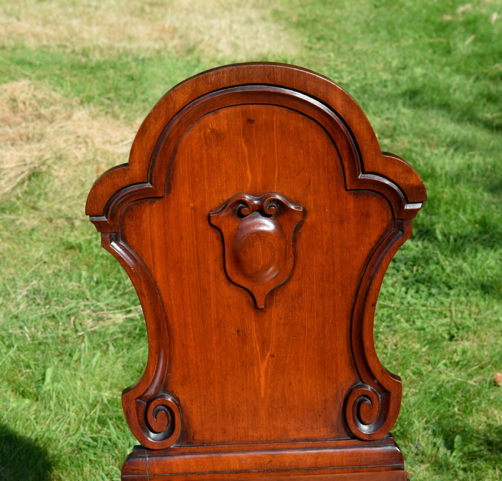 A Victorian mahogany hall chair with a carved shield-shaped backrest, stud-trimmed dark seat, turned front legs, and splayed rear legs. View XII