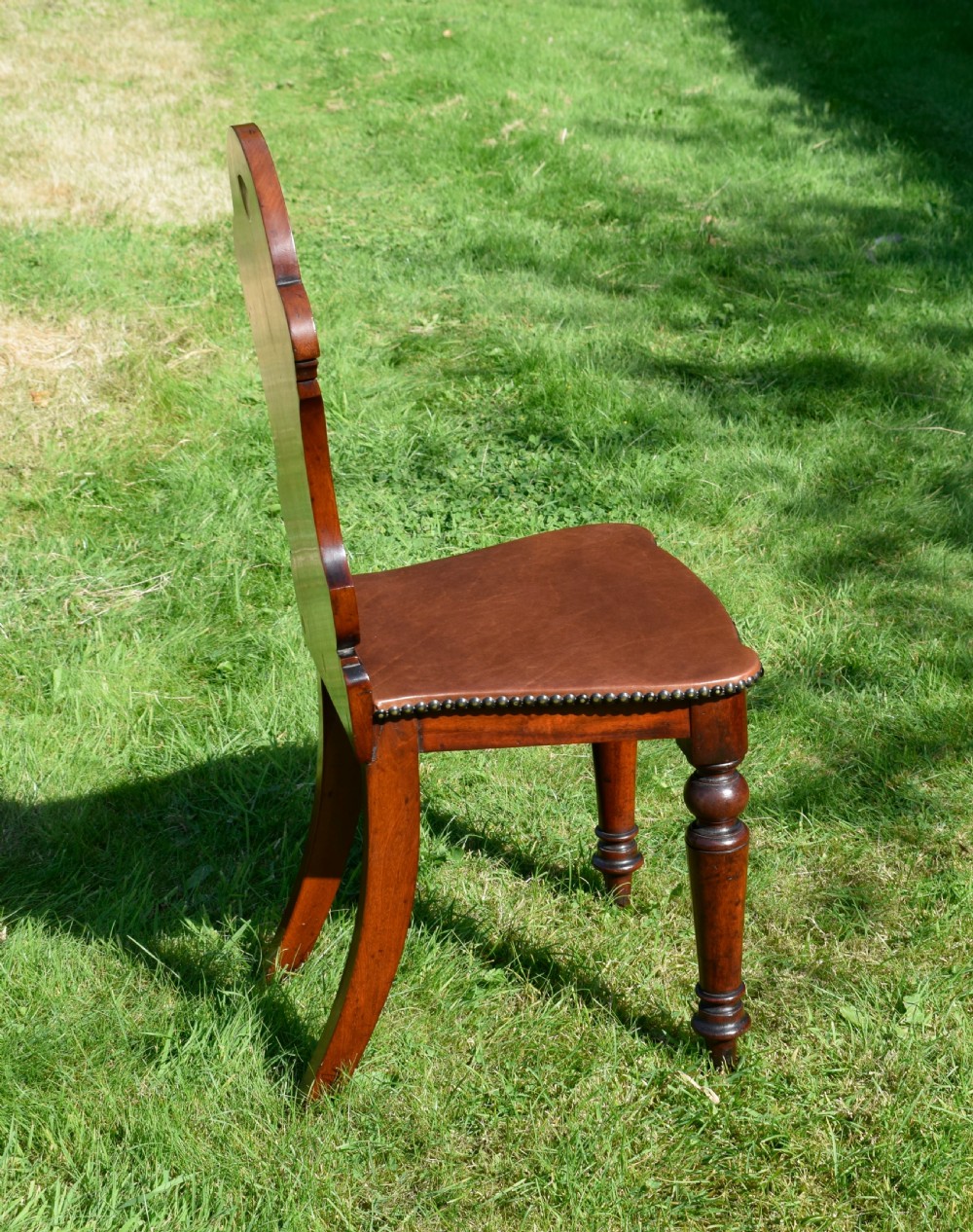 A Victorian mahogany hall chair with a carved shield-shaped backrest, stud-trimmed dark seat, turned front legs, and splayed rear legs. View XIII