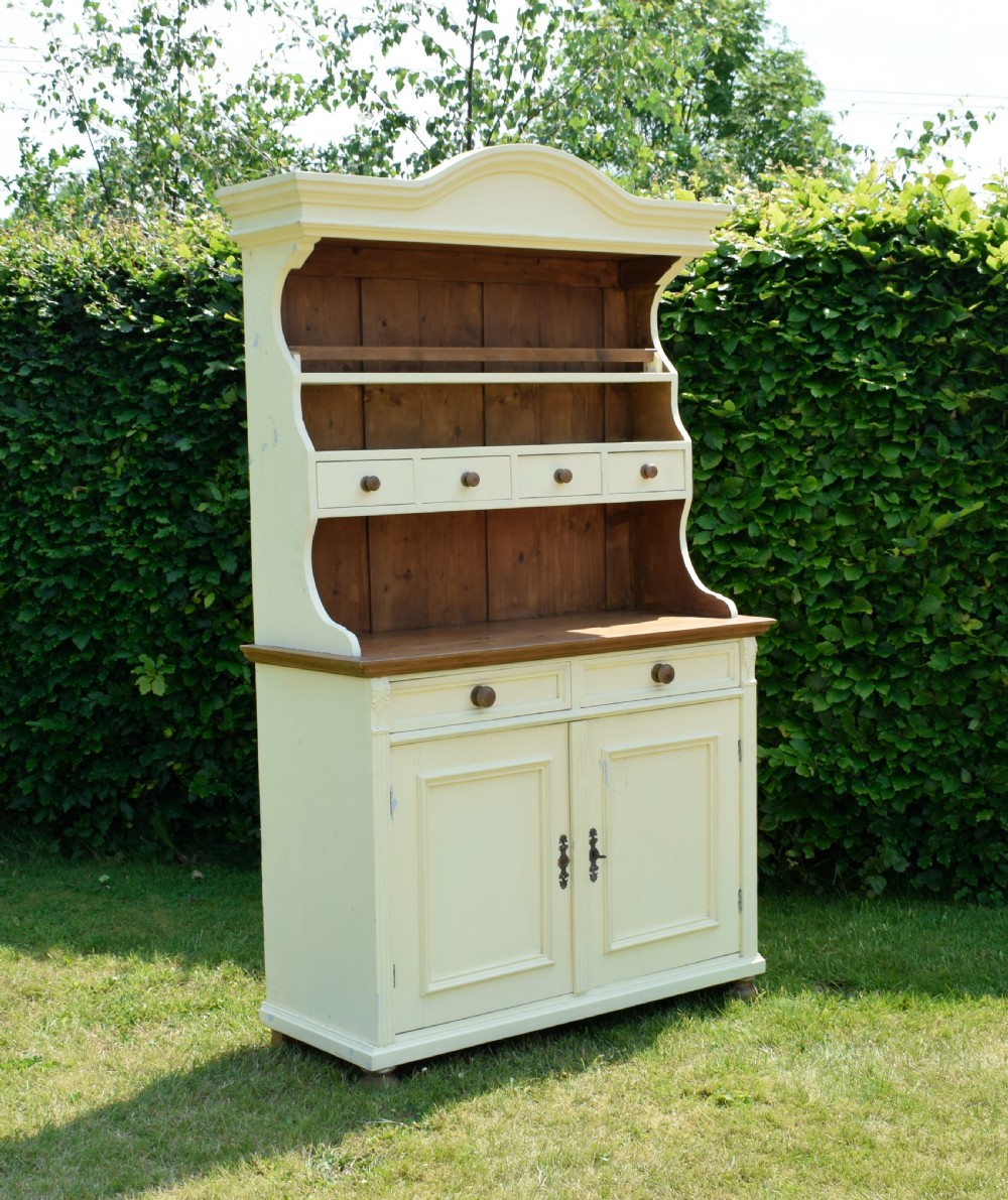 An early twentieth-century painted cream pine kitchen dresser featuring an upper shelf rack with small drawers over a two-door base cupboard.