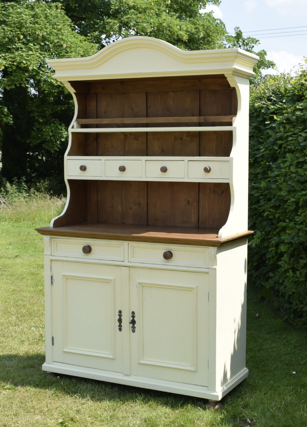 An early twentieth-century painted cream pine kitchen dresser featuring an upper shelf rack with small drawers over a two-door base cupboard. View II
