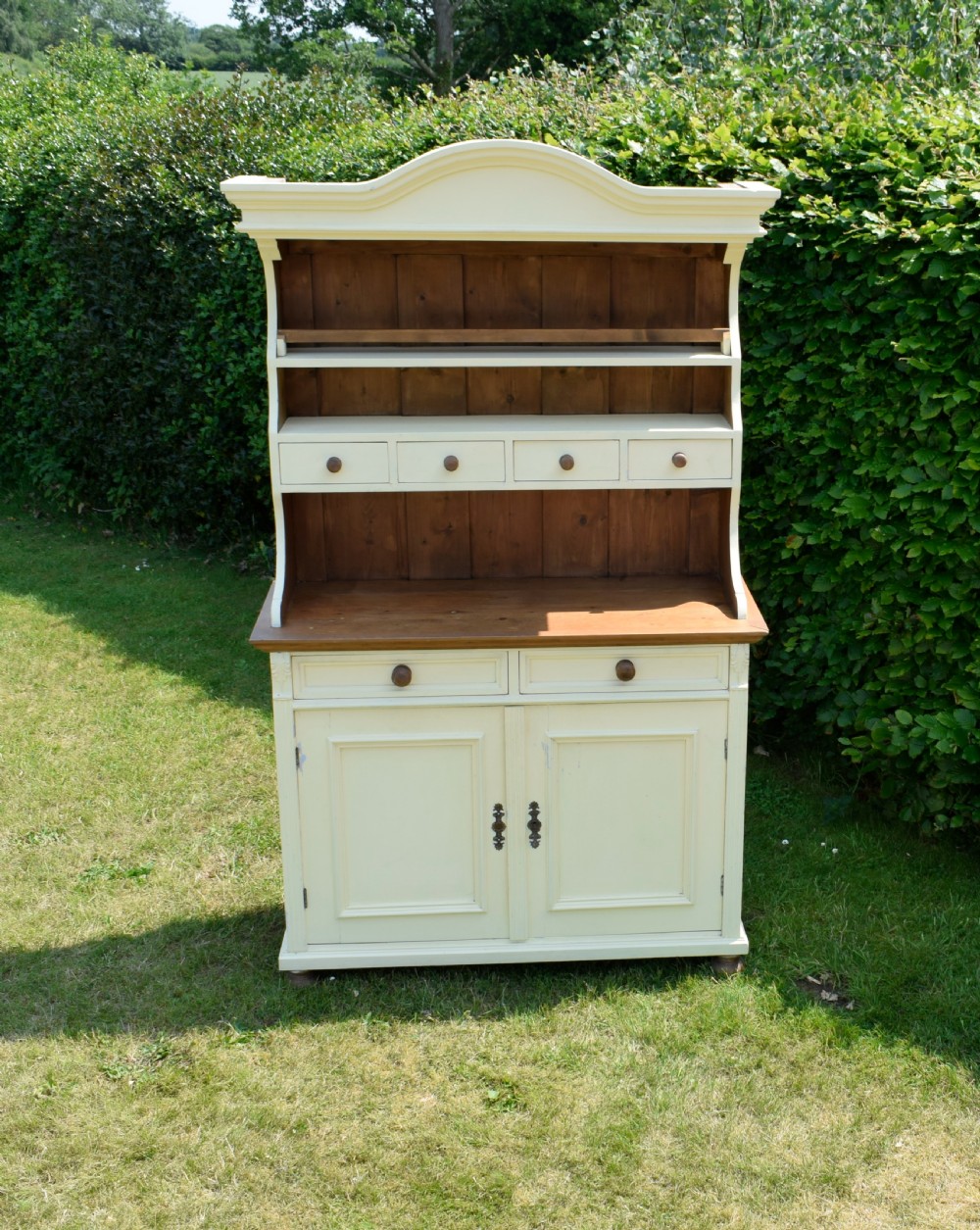 An early twentieth-century painted cream pine kitchen dresser featuring an upper shelf rack with small drawers over a two-door base cupboard. View V