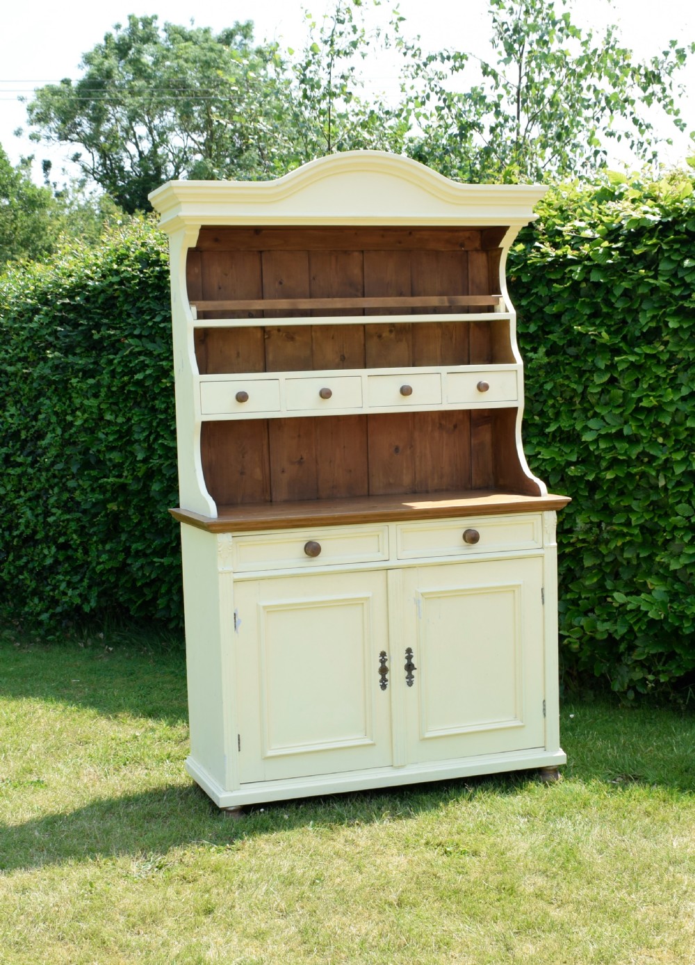 An early twentieth-century painted cream pine kitchen dresser featuring an upper shelf rack with small drawers over a two-door base cupboard. View VI