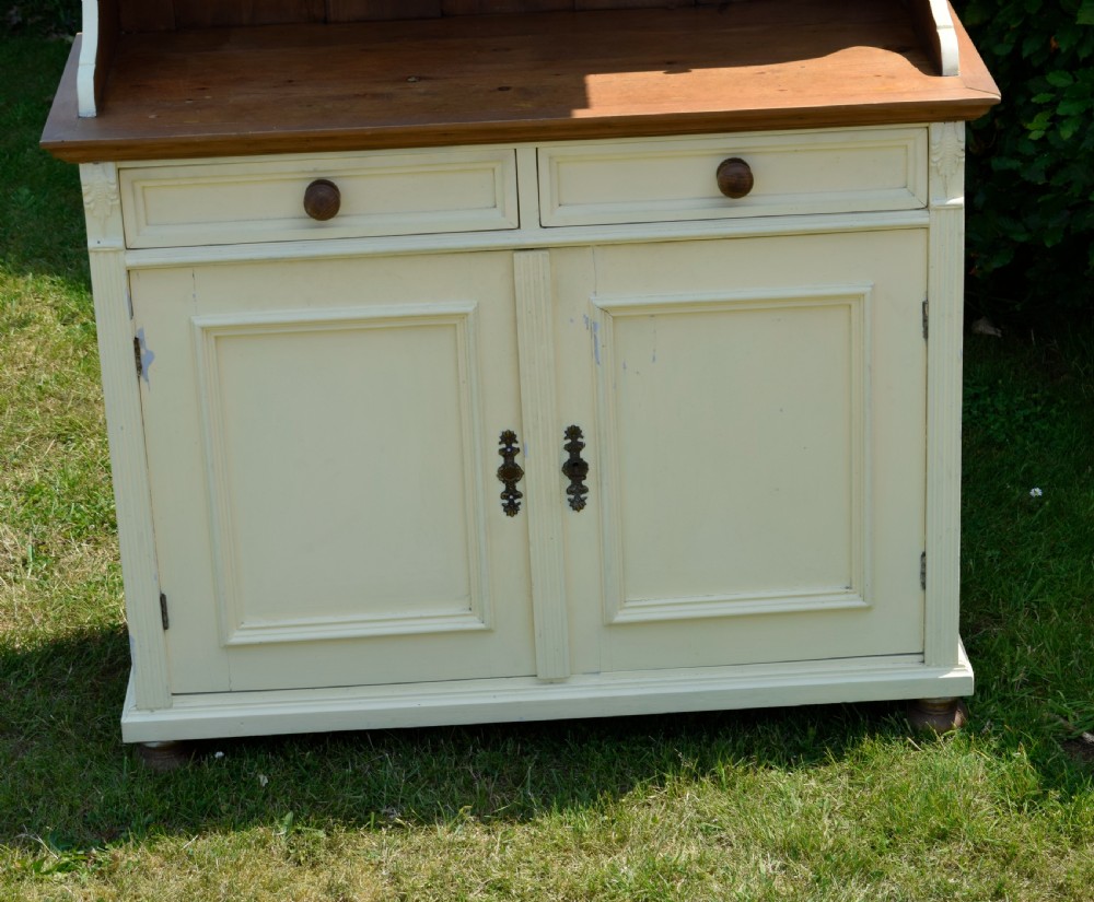An early twentieth-century painted cream pine kitchen dresser featuring an upper shelf rack with small drawers over a two-door base cupboard. View IX