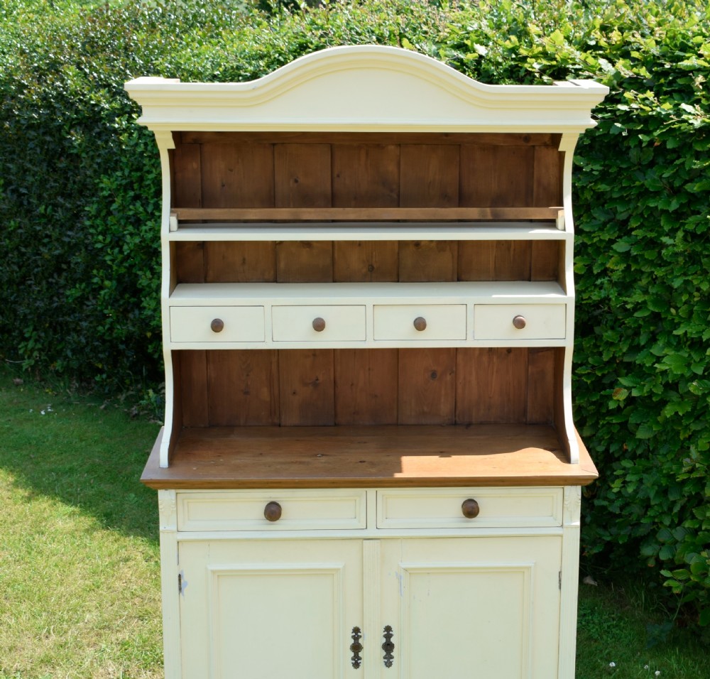 An early twentieth-century painted cream pine kitchen dresser featuring an upper shelf rack with small drawers over a two-door base cupboard. View X