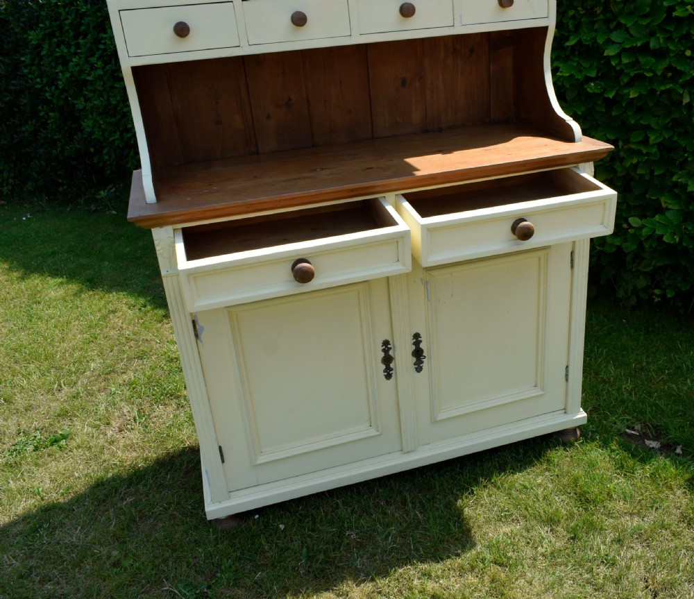 An early twentieth-century painted cream pine kitchen dresser featuring an upper shelf rack with small drawers over a two-door base cupboard. View XIV