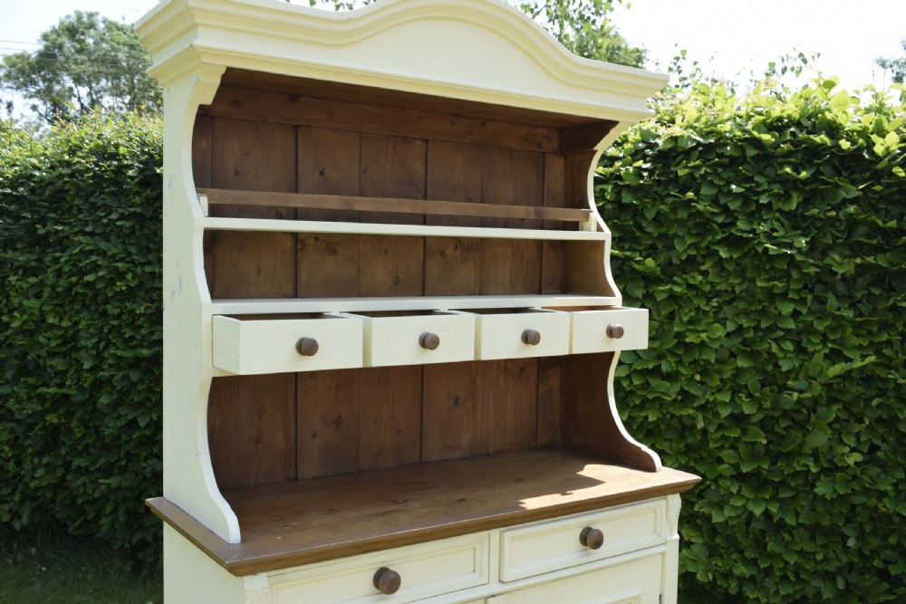 An early twentieth-century painted cream pine kitchen dresser featuring an upper shelf rack with small drawers over a two-door base cupboard. View XV