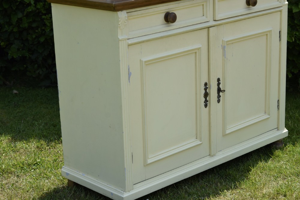 An early twentieth-century painted cream pine kitchen dresser featuring an upper shelf rack with small drawers over a two-door base cupboard. View XX