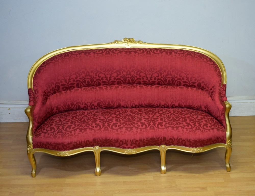 An antique French canape settee with a carved gold-gilded frame, cabriole legs, and red patterned damask upholstery. View V