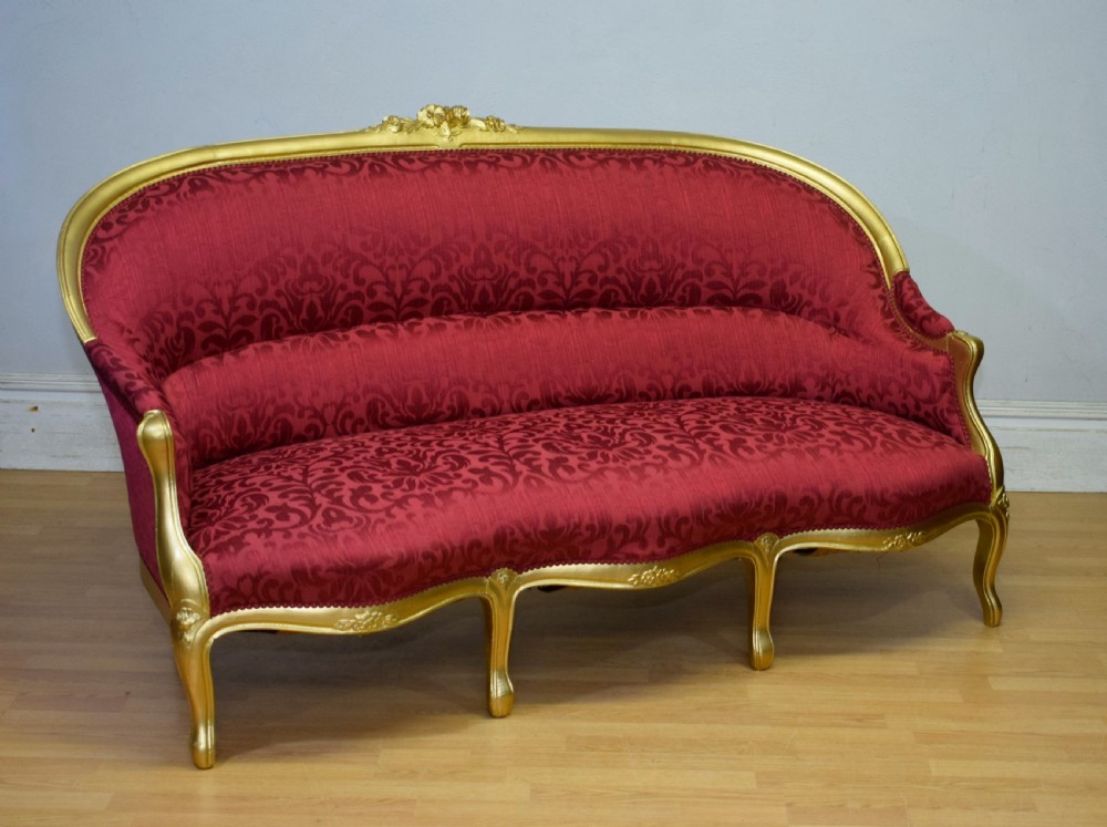An antique French canape settee with a carved gold-gilded frame, cabriole legs, and red patterned damask upholstery. View X
