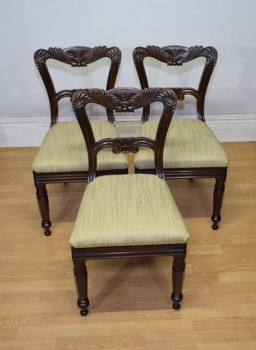 Set of three Scottish Regency mahogany dining chairs featuring carved crest rails, scrolled open backs, turned front legs, and pale green upholstered seats.