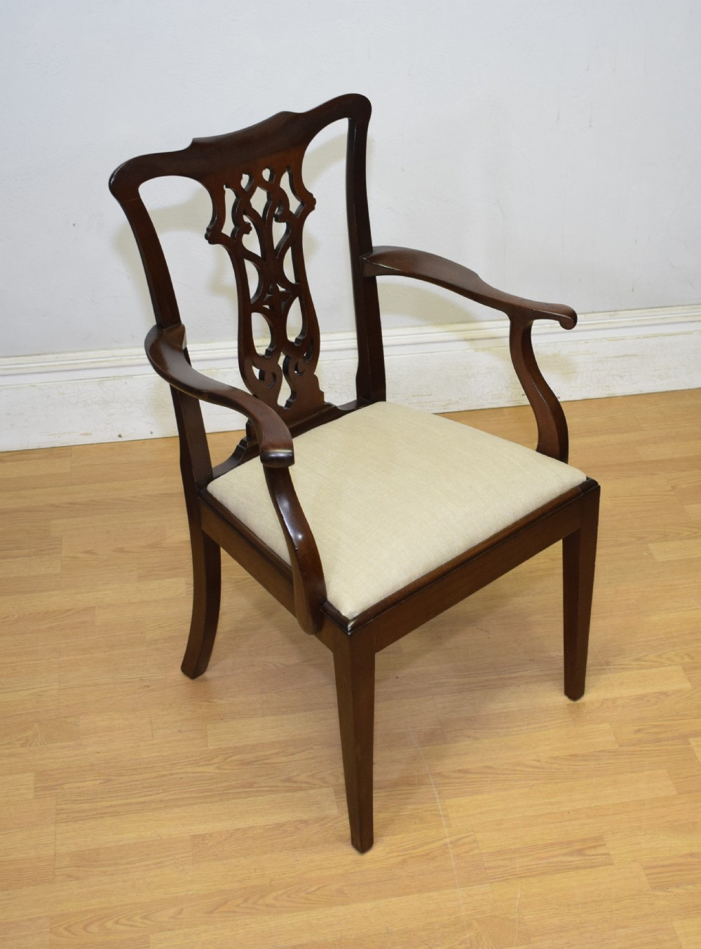A 19th-century mahogany open armchair featuring a carved pierced back splat, curved arms, and a neutral cream upholstered seat.