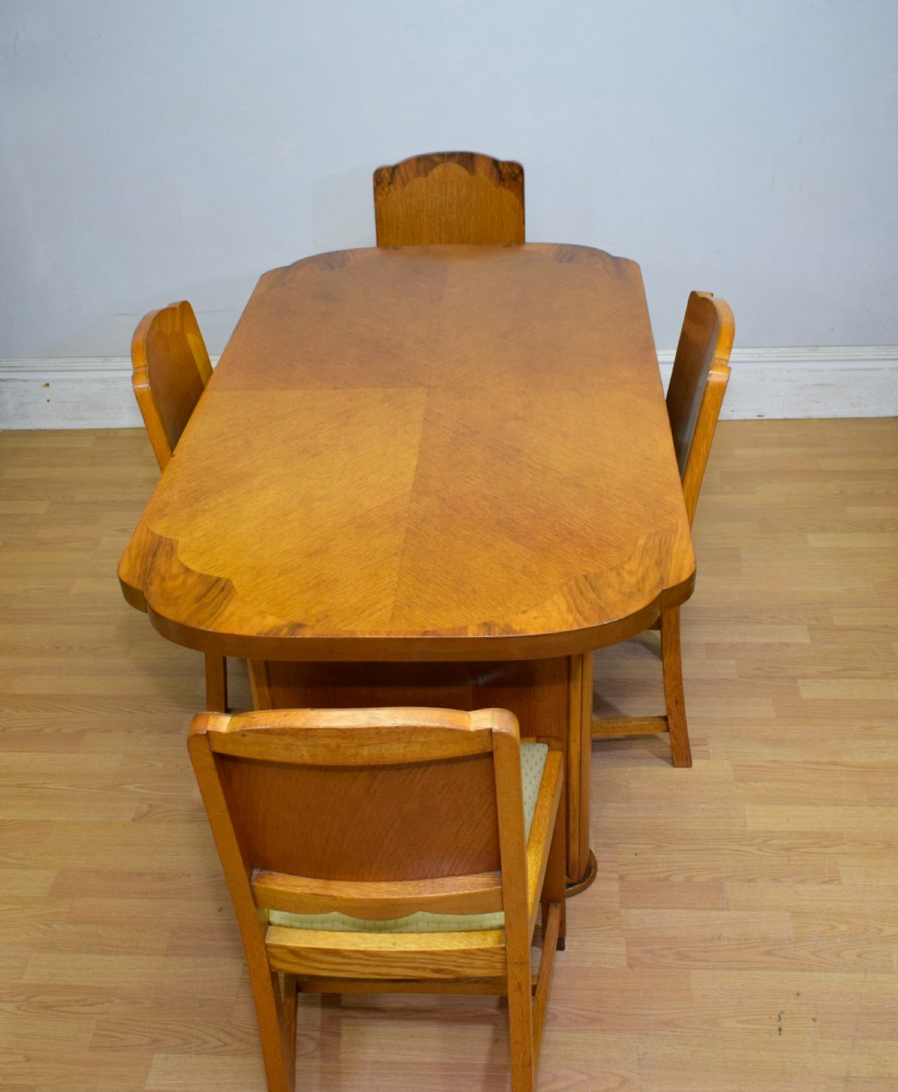 An Art Deco light oak dining suite featuring a shaped table with a central pedestal surrounded by four matching upholstered chairs. View V