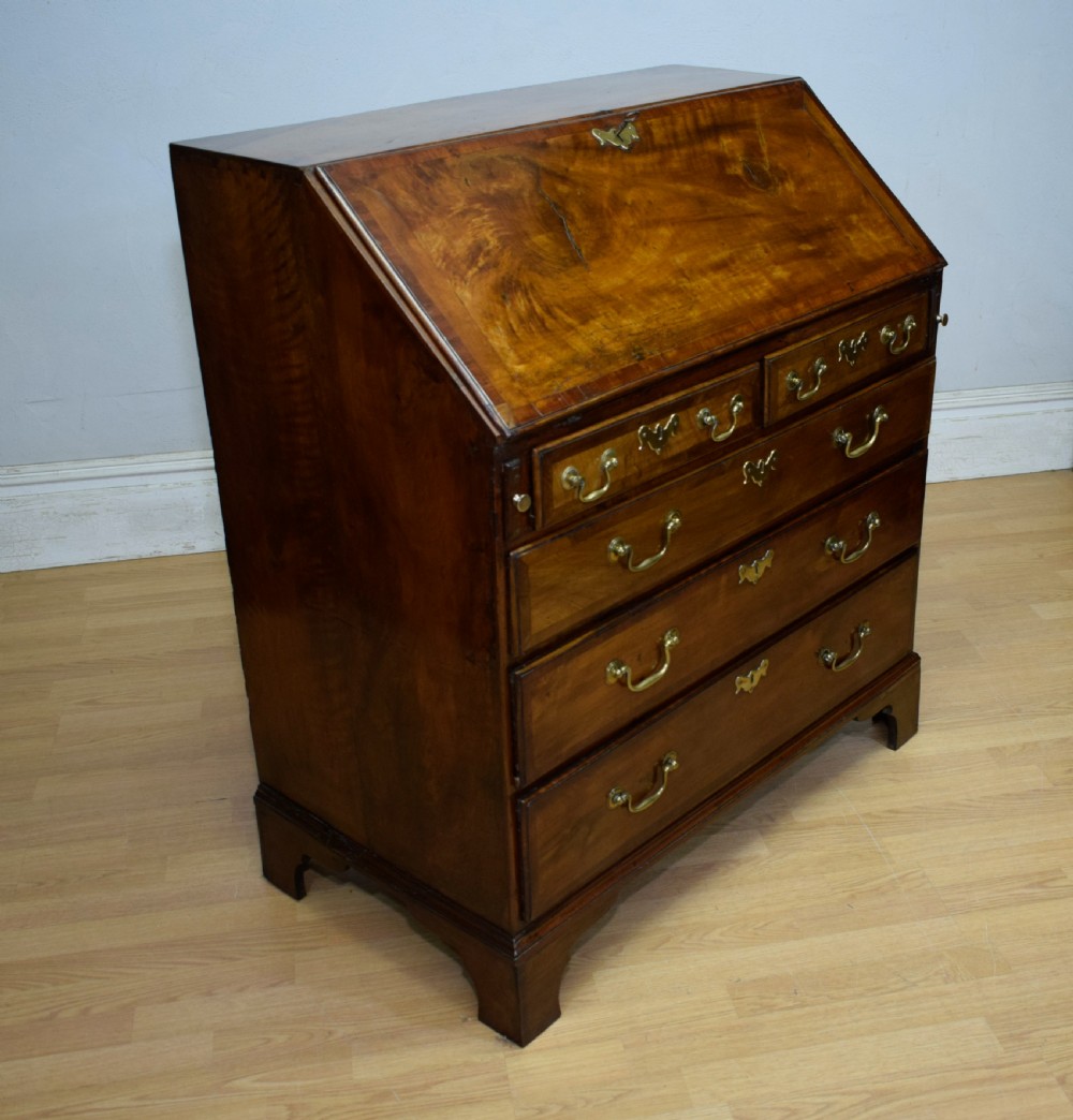 A Georgian walnut bureau featuring a sloped hinged front opening above four graduated drawers with decorative brass handles and bracket feet.