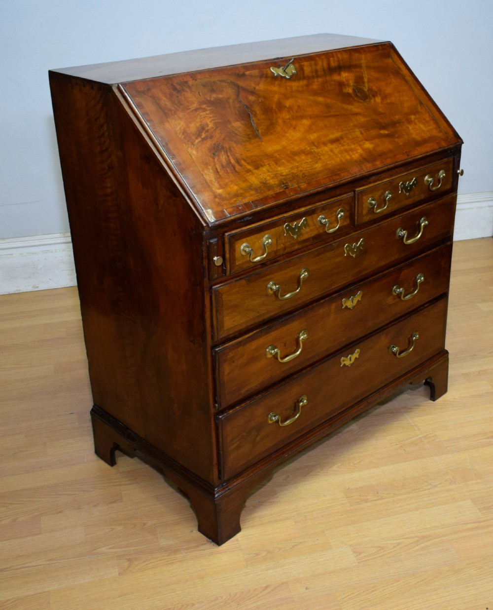 A Georgian walnut bureau featuring a sloped hinged front opening above four graduated drawers with decorative brass handles and bracket feet. View II