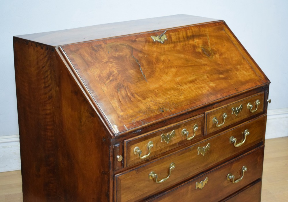 A Georgian walnut bureau featuring a sloped hinged front opening above four graduated drawers with decorative brass handles and bracket feet. View III