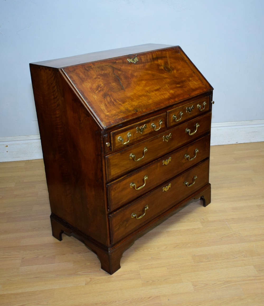A Georgian walnut bureau featuring a sloped hinged front opening above four graduated drawers with decorative brass handles and bracket feet. View V