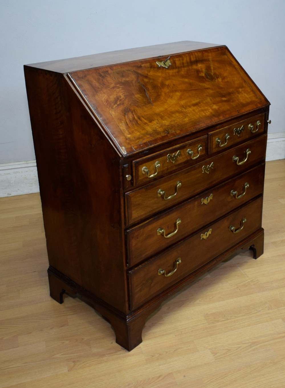 A Georgian walnut bureau featuring a sloped hinged front opening above four graduated drawers with decorative brass handles and bracket feet. View VI