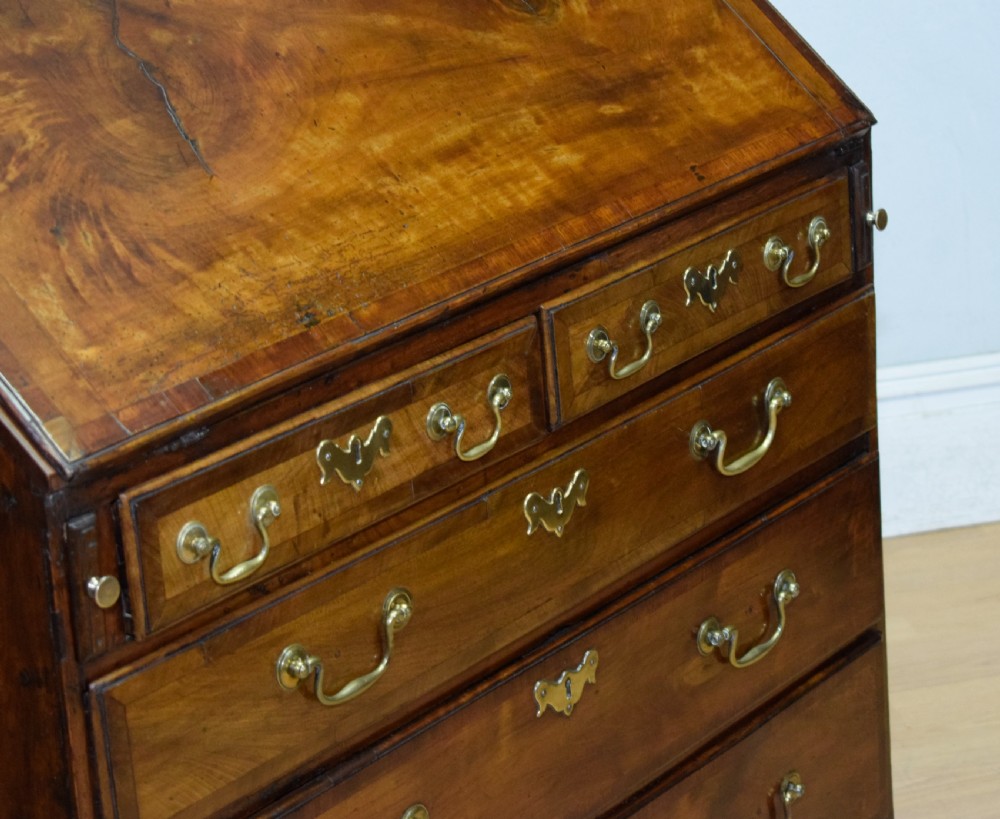 A Georgian walnut bureau featuring a sloped hinged front opening above four graduated drawers with decorative brass handles and bracket feet. View VII